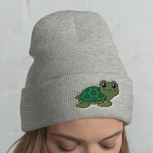 May include: Gray beanie with a green turtle graphic on the front. The turtle has a smiling face and is wearing a shell.