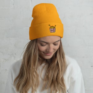 May include: A yellow beanie with a red and white striped popcorn bucket embroidered on the front.