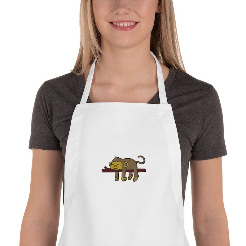 May include: White kitchen apron with a brown monkey sleeping on a branch embroidered on the front.