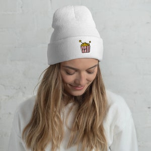 May include: White beanie with a red and white striped popcorn bucket with yellow popcorn embroidered on the front.