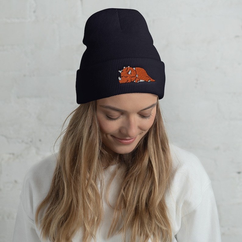 Puede incluir: Un gorro negro con un dinosaurio marr&oacute;n bordado en la parte delantera. El gorro est&aacute; hecho de un material suave y c&aacute;lido, perfecto para mantener la cabeza caliente en invierno.
