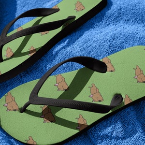 May include: A pair of green flip flops with a cartoon dog print. The flip flops have black straps.