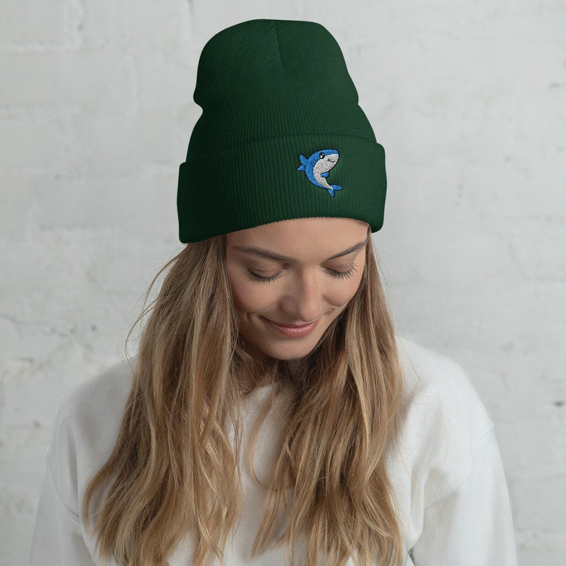 May include: A dark green beanie with a blue and white cartoon shark embroidered on the front.