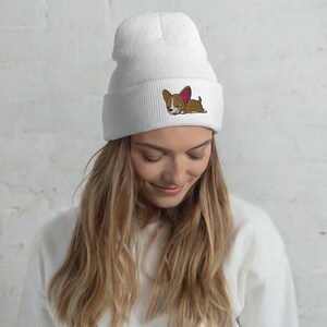 May include: White beanie with a brown and white cartoon dog embroidered on the front. The dog has pink ears and is lying down.