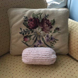 Puede incluir: Una almohada de crochet blanca con una almohada bordada con flores detrás en un sofá de estampado amarillo.