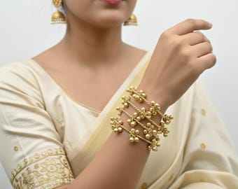May include: A set of gold-toned metal bangles featuring a twisted wire design adorned with small, dangling spherical charms. The bracelets are worn on the wrist, showcasing a metallic finish and a delicate, intricate structure with multiple hanging beads.