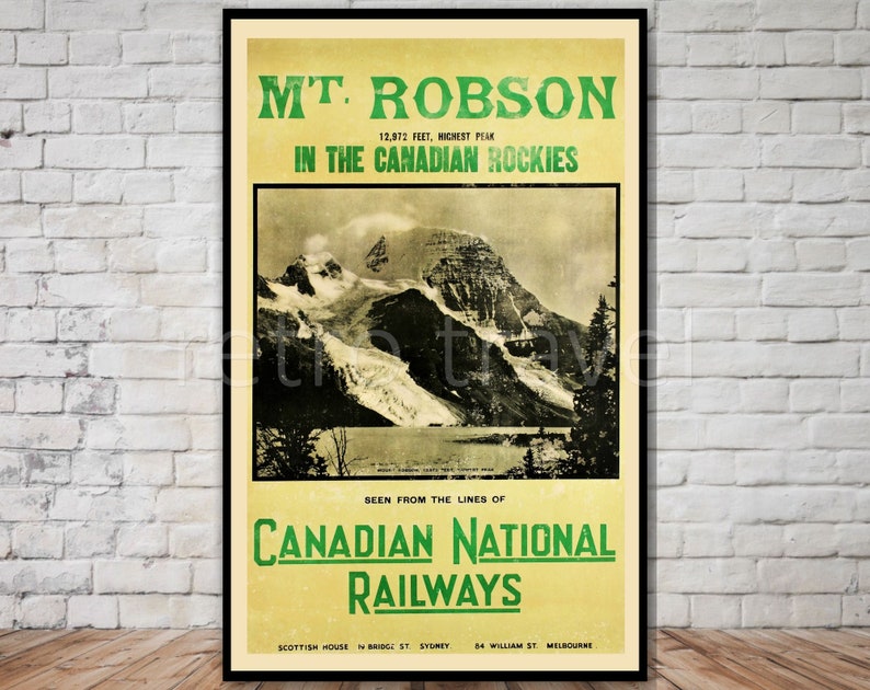 May include: Vintage travel poster advertising a trip to see Mount Robson in the Canadian Rockies. The poster features a black and white photo of the mountain with a glacier and a lake in the foreground. The text on the poster reads "M'T. ROBSON 12,972 FEET, HIGHEST PEAK IN THE CANADIAN ROCKIES SEEN FROM THE LINES OF CANADIAN NATIONAL RAILWAYS SCOTTISH HOUSE ST. SYDNEY. 84 WILLIAM ST. MELBOURNE."