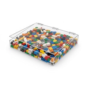 May include: A clear acrylic storage box filled with colorful plastic building blocks. The blocks are various sizes and colors, including red, blue, yellow, green, and white. The box has a hinged lid and is sitting on a white surface.