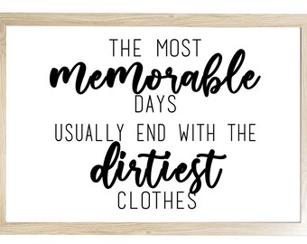 May include: A framed print with a light wood grain border. The white background features black cursive text that reads: "THE MOST memorable DAYS USUALLY END WITH THE dirtiest CLOTHES."