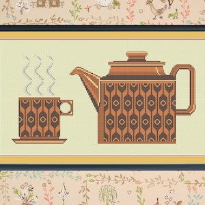 Può includere: Un ricamo a punto croce incorniciato di una teiera marrone e una tazza da tè marrone con un piattino. La teiera e la tazza da tè hanno un motivo geometrico in marrone e nero.