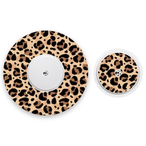 Peut inclure: Deux couvercles adhésifs à imprimé léopard pour un appareil médical. Le plus grand couvercle est rond et comporte un petit trou au centre. Le plus petit couvercle est également rond et comporte un trou similaire au centre.