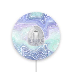 May include: A round wall decor with a swirling blue, purple, and green marble pattern. The decor has a white, glittery finish and a white plug.