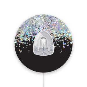 Op de afbeelding: Een ronde sticker in zwart en wit met een doorzichtige plastic haak. De sticker heeft een ontwerp van iriserende glitter op een zwarte achtergrond.