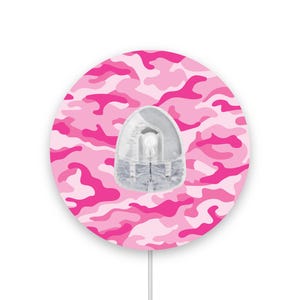 May include: A round pink and white camouflage patterned wall outlet cover with a clear plastic outlet insert.