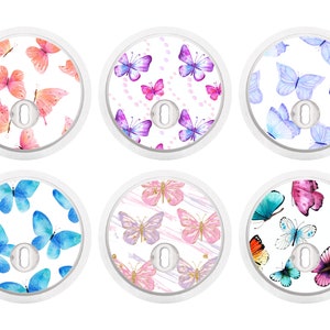 Puede incluir: Seis pegatinas redondas blancas con diferentes diseños de mariposas. Cada pegatina presenta un patrón de mariposa de acuarela con varios colores, incluidos el rosa, el azul, el morado y el dorado. Las pegatinas están diseñadas para colocarse en una superficie redonda blanca.