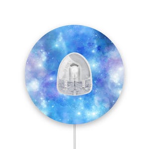 Peut inclure: Un tapis de souris rond avec un motif de galaxie en bleu, violet et blanc. Le tapis de souris a une découpe de souris blanche au centre.