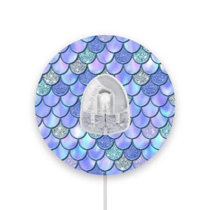 May include: A round, blue and silver mermaid scale patterned wall plate with a clear plastic outlet cover in the centre.