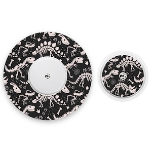 May include: Two round adhesive bandages with a black background and a white dinosaur skeleton pattern. The larger bandage has a white center circle with a small hole in the middle.