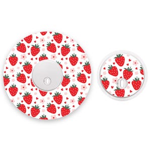Może przedstawiać: Dwa okrągłe białe osłony przełączników światła z wzorem czerwonych i białych truskawek. Większa osłona ma białe centrum z małym otworem w środku.