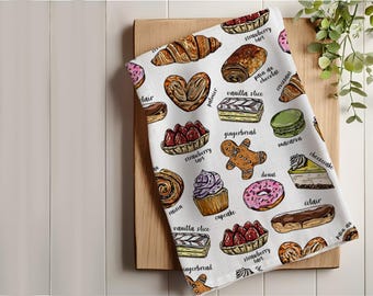 May include: White kitchen towel with a colorful illustration of various pastries and desserts, including a strawberry tart, a pain au chocolat, a vanilla slice, a gingerbread man, a macaron, a donut, a cupcake, a cheesecake, and a éclair. The text on the towel includes the names of each pastry in English.