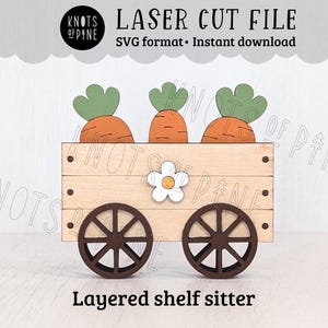 May include: Wooden layered shelf sitter featuring a cart with three carrots and green tops. The cart has two brown wheels and a white flower. The text "LASER CUT FILE" and "Layered shelf sitter" are visible.