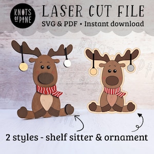 Puede incluir: Dos estilos de adornos de reno cortados con láser. Un reno está sentado con las piernas estiradas, el otro está de pie con las piernas dobladas. Ambos renos tienen bufandas a rayas rojas y blancas y adornos dorados y plateados colgando de sus cuernos.