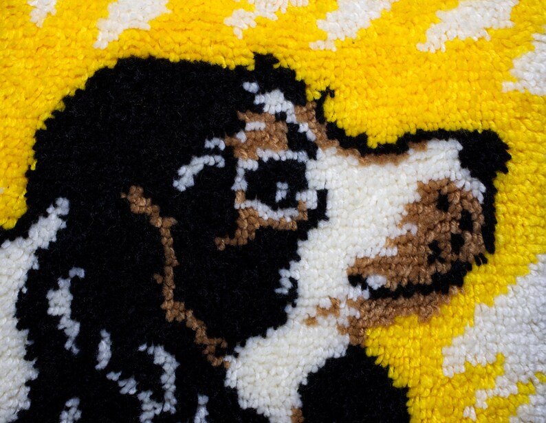 May include: A close-up of a handmade rug depicting a dog's face. The dog has black, white, and brown fur, set against a yellow and white background. The rug is made with a textured, looped pile.