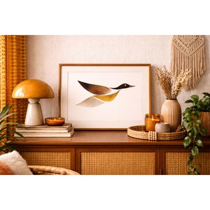 May include: A wooden cabinet with a framed art print of a bird in flight, a mushroom-shaped lamp, candles, and a vase with dried flowers. The art print features brown, black, and gold tones. The scene is decorated in warm, earthy tones.