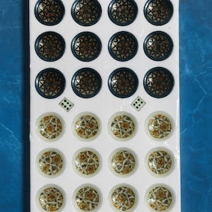 May include: A sheet of decorative, round embellishments. The top row features dark blue circles with gold and black patterns. The bottom row has off-white circles with a brown and gold design. The embellishments are on a white background.