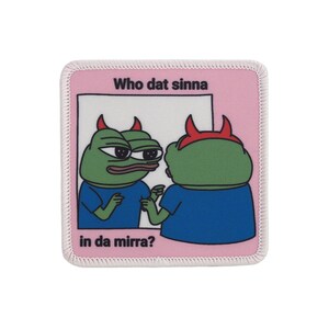 Pode incluir: Um remendo rosa e branco com um sapo verde de desenho animado olhando para um espelho. O texto no remendo diz "Who dat sinna in da mirra?"