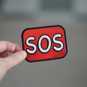 May include: Red fabric patch with black stitching and white embroidered letters spelling "SOS".