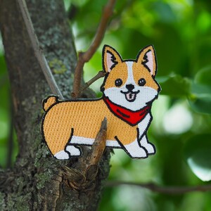 Könnte beinhalten: Ein gestickter Aufnäher mit einem Cartoon-Corgi, der ein rotes Bandana trägt. Der Corgi lächelt und hat eine weiße Brust.