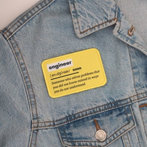 Könnte beinhalten: Gelber Stoff-Patch mit dem Wort "engineer" definiert als "Jemand, der Probleme löst, von denen Sie nicht wussten, dass sie existieren, auf eine Weise, die Sie nicht verstehen."