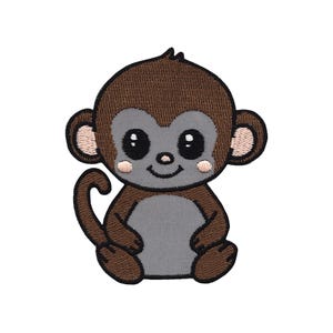 Könnte beinhalten: Ein brauner und grauer Cartoon-Affe mit großen Augen und einem Lächeln. Der Affe sitzt mit gekreuzten Beinen und verschränkten Armen.