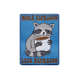 以下が含まれることがあります： コーヒーカップを持ったアライグマが描かれた青い刺繍パッチ。パッチには「More Espresso Less Depresso」という文字が書かれています。