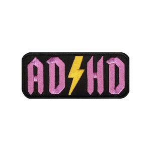 May include: Pink embroidered patch with the text "ADHD" in a bold, stylized font. A yellow lightning bolt is centred between the "D" and "H".
