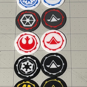 May include: A collection of ten circular tokens featuring various designs in white, black, red, blue, and yellow. The tokens have different geometric and symbol designs, including stars, triangles, and other shapes.
