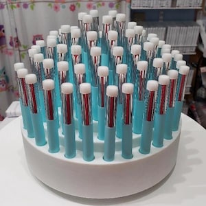 May include: A display of makeup applicators. Each applicator has a white sponge tip, a silver metal shaft, and a light blue handle. The applicators are arranged in a white, circular holder.