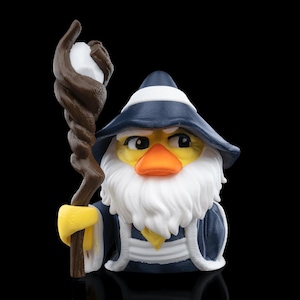 May include: A whimsical figurine of a duck dressed as a wizard, featuring a blue hat with a white band, a white beard, and a blue robe. The duck holds a brown staff with a white orb.