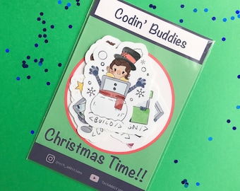 Może przedstawiać: Przezroczysta plastikowa koperta zawierająca zestaw naklejek z napisami Codin' Buddies oraz Christmas Time!!. Naklejki przedstawiają postać z kreskówki w cylindrze i szaliku, wyłaniającą się z bałwana z tagami kodu <BUILD/> i <GN/>.