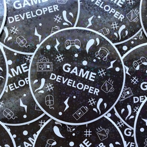 May include: A collection of round stickers with a black background and white graphics. Each sticker has the words "GAME DEVELOPER" in large white letters. The stickers feature icons of game controllers, computer mice, and coffee mugs.