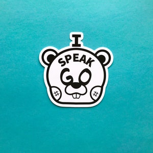 May include: A white sticker with a black outline of a cartoon bear face. The bear has the text "I SPEAK GO" in black letters. The sticker is on a teal background.