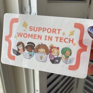 May include: A rectangular sticker with the text "SUPPORT WOMEN IN TECH" in orange. The sticker shows illustrations of five women using laptops. The design includes orange brackets and yellow diamond shapes.