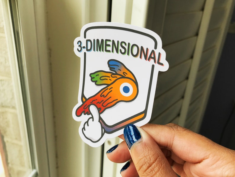 May include: A sticker with the text "3-DIMENSIONAL" in rainbow colors. The sticker features a stylized orange, yellow, and blue design with a white hand pointing at it. The sticker is held by a person.