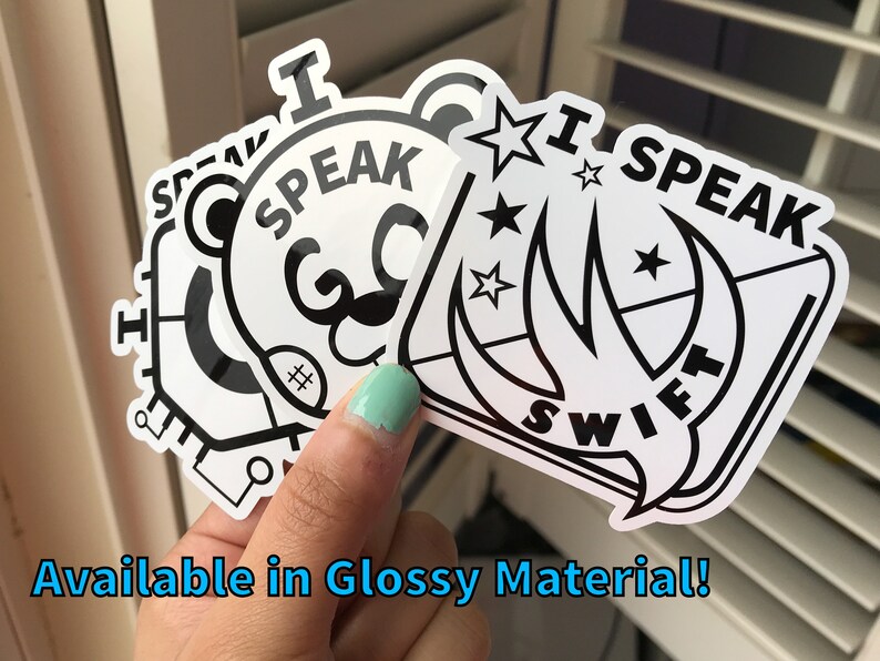 May include: A hand holds several white stickers with black text and designs. The stickers say "I SPEAK SWIFT" and "I SPEAK" with a bear face. The text "Available in Glossy Material!" is at the bottom.