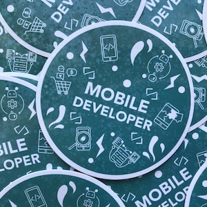 May include: A collection of round, teal stickers with the words "MOBILE DEVELOPER" in white. The stickers feature white icons of coding symbols, shopping carts, and mobile phones. The background has a subtle snowflake pattern.