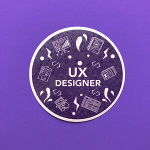 Op de afbeelding: Een paarse cirkel met witte pictogrammen en de tekst "UX DESIGNER" in het midden. De pictogrammen omvatten een kalender, een website, een notitieboekje, een telefoon en een gebruikersprofiel.