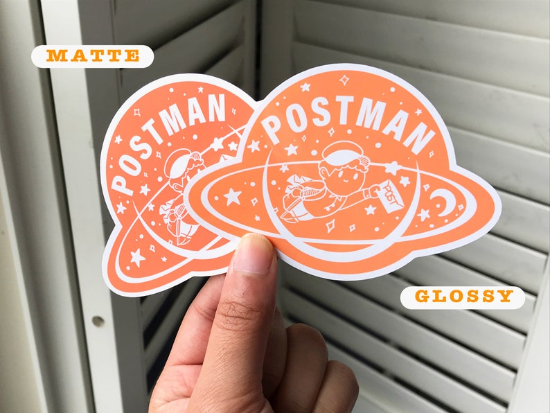 K&ouml;nnte beinhalten: Zwei orangefarbene Aufkleber mit wei&szlig;em Rand. Die Aufkleber zeigen eine Comicfigur in einem Raumanzug, die einen Brief mit der Aufschrift "Post" h&auml;lt. Der Text "POSTMAN" ist in einem wei&szlig;en Kreis um die Figur geschrieben. Ein Aufkleber ist mit "Matt" und der andere mit "Glanz" beschriftet.