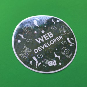Pode incluir: Um autocolante redondo e hologr&aacute;fico com a inscri&ccedil;&atilde;o "WEB DEVELOPER" em branco. Apresenta &iacute;cones brancos relacionados com o desenvolvimento web, como uma l&acirc;mpada, par&ecirc;nteses de c&oacute;digo e um computador. O fundo &eacute; verde vibrante.