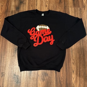 May include: Black sweatshirt with a red "Game Day" graphic and a brown football.